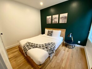 Een slaapkamer met een bed, nachtkastje, lamp en wanddecoratie.