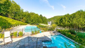 Un jardin avec deux piscines, une terrasse en pierre et un espace clos avec une chaise.