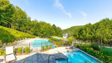 Un jardin avec deux piscines, une terrasse en pierre et un espace clos avec une chaise.