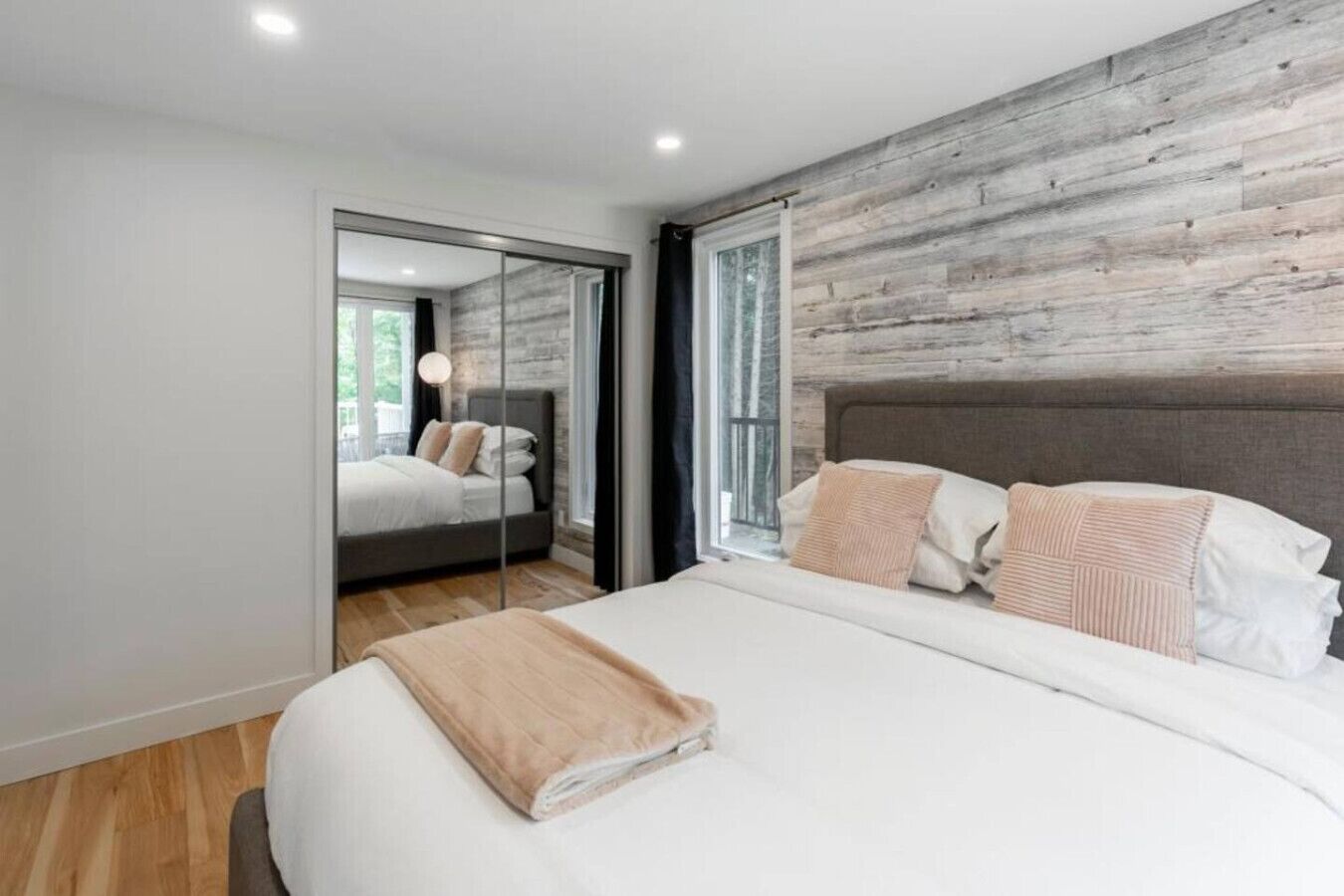 Un dormitorio moderno con una cama grande, una pared de acento de madera y un espejo que refleja la habitación.