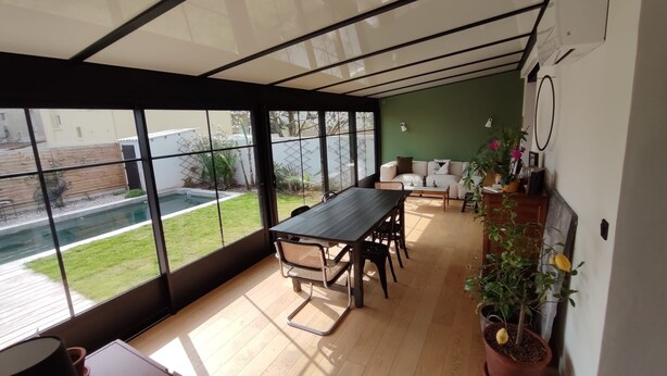 Un interior moderno con un gran ventanal, una mesa de comedor de madera y una pared verde.