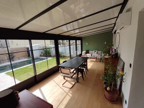 A modern interior with a large glass window, a wooden dining table, and a green wall. - Villa avec piscine proche décentré-ville. (Montpellier)
