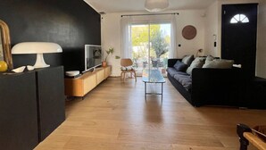 Una sala moderna con un sofá negro, una mesa de centro de vidrio y un mueble de madera.