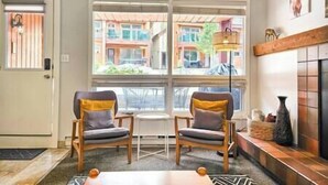 A room with two wooden chairs, a small round table, and a view of buildings outside through large windows. - Beautiful one bedroom condo at Horsethief Lodge (Panorama)