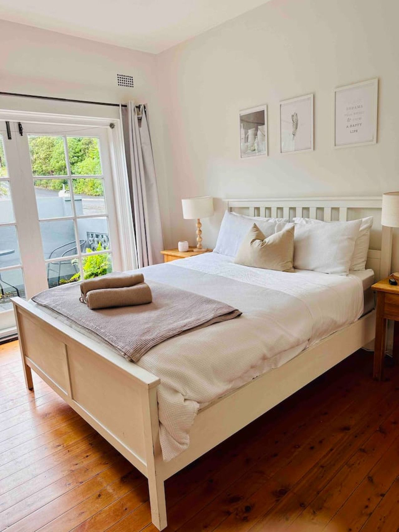 A bedroom with a large bed, a window with curtains, a nightstand, and a wall with framed pictures.