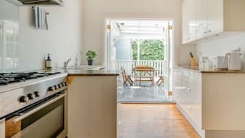 A kitchen with a gas stove, sink, and cabinets. There is a dining area with a table and chairs, and a view of greenery outside.