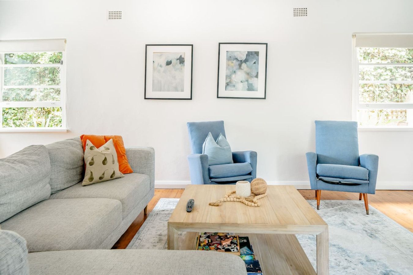 A living room with a grey sofa, two blue armchairs, a wooden coffee table, and abstract art on the wall.