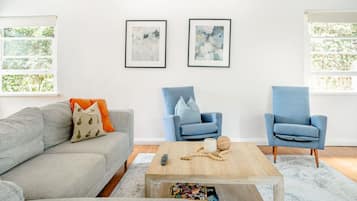 A living room with a grey sofa, two blue armchairs, a wooden coffee table, and abstract art on the wall.