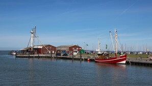 Un puerto con un barco rojo amarrado, un edificio con un letrero que dice "Fisch" y una estructura de grúa.