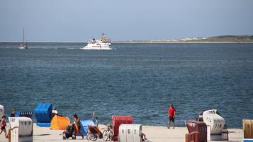 Ein Strand mit Liegestühlen und Sonnenschirmen, ein Boot im Wasser und ein sandiger Uferstreifen.