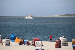 A beach with beach chairs and umbrellas, a boat in the water, and a sandy shore.