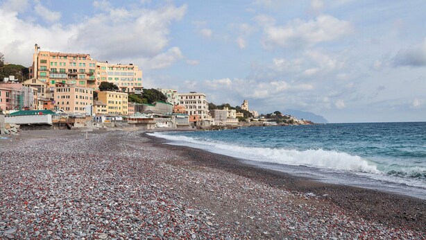 A pebble beach with buildings in the background. - L'Aria del Mare by Wonderful Italy (Genoa)