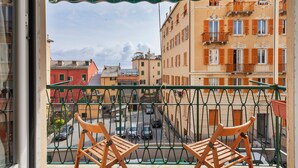 A balcony with two wooden chairs, a view of a street with parked cars, and buildings with balconies and shutters. - L'Aria del Mare by Wonderful Italy (Genoa)