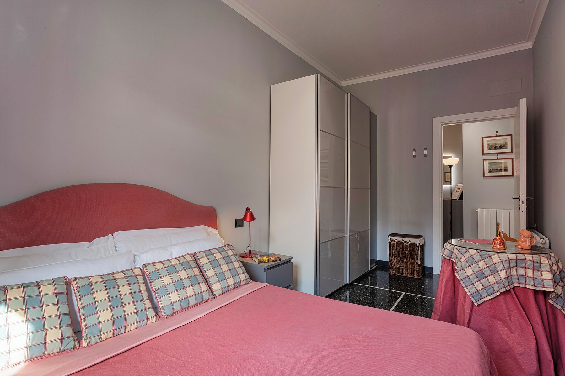 A bedroom with a bed, a nightstand, a dresser, a mirror, and a door leading to another room.