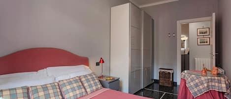 A bedroom with a bed, a nightstand, a dresser, a mirror, and a door leading to another room.