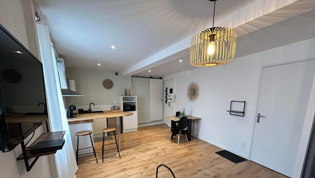 Une cuisine moderne avec un plan de travail en bois, des tabourets de bar et un luminaire suspendu.