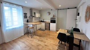 Une cuisine compacte dotée d’un plan de travail en bois, d’un évier, d’un four à micro-ondes et d’un petit réfrigérateur. On y trouve deux tabourets et une table à manger avec des chaises.