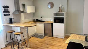 Une cuisine compacte dotée d’un plan de travail en bois, d’un évier, d’un four à micro-ondes et d’un petit réfrigérateur. On y trouve deux tabourets et une table à manger avec un set de table.