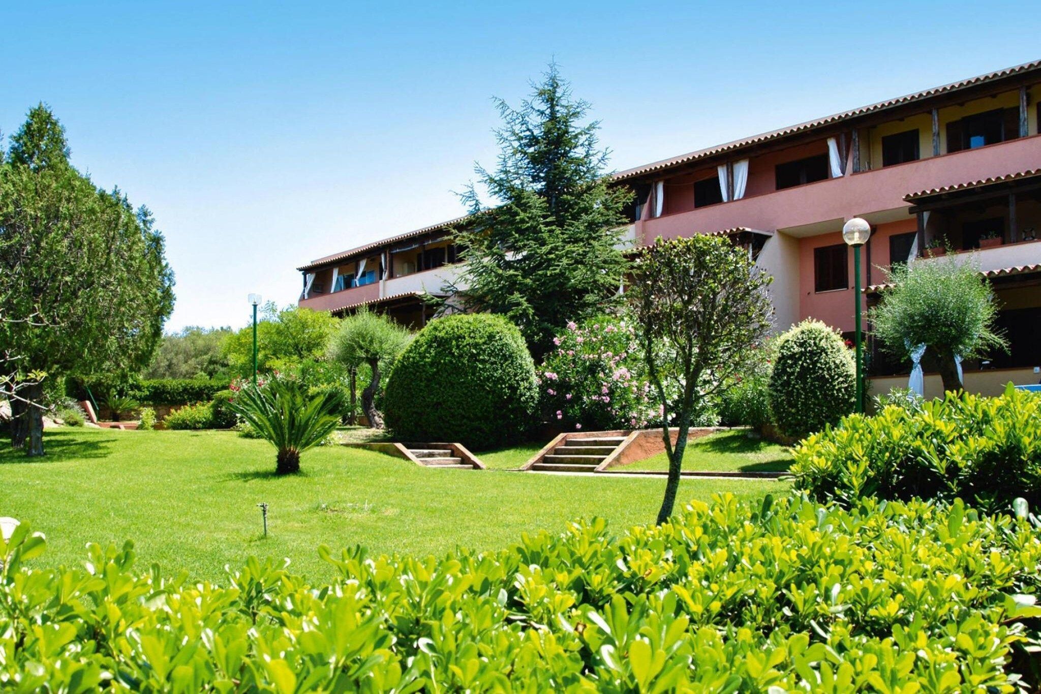 Un hotel con un jardín bien cuidado, que incluye céspedes cuidados y diversos arbustos.
