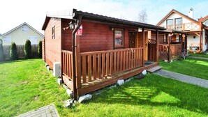 A wooden cabin with a porch, a small front yard, and a neighboring house.
