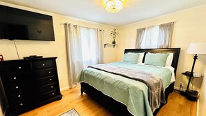 Ein Schlafzimmer mit einem Bett, einem Schminktisch, einem an der Wand befestigten Fernseher und einer Lampe.