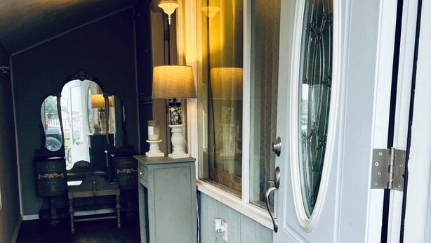 Ein Flur mit Holzboden, einer weißen Tür mit Fenster, einem kleinen Tisch mit Lampe und einem Spiegel an der Wand.
