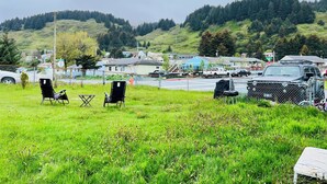 Eine Wiese mit einigen Stühlen, einem kleinen Tisch, einem Zaun und einem parkenden Lastwagen.