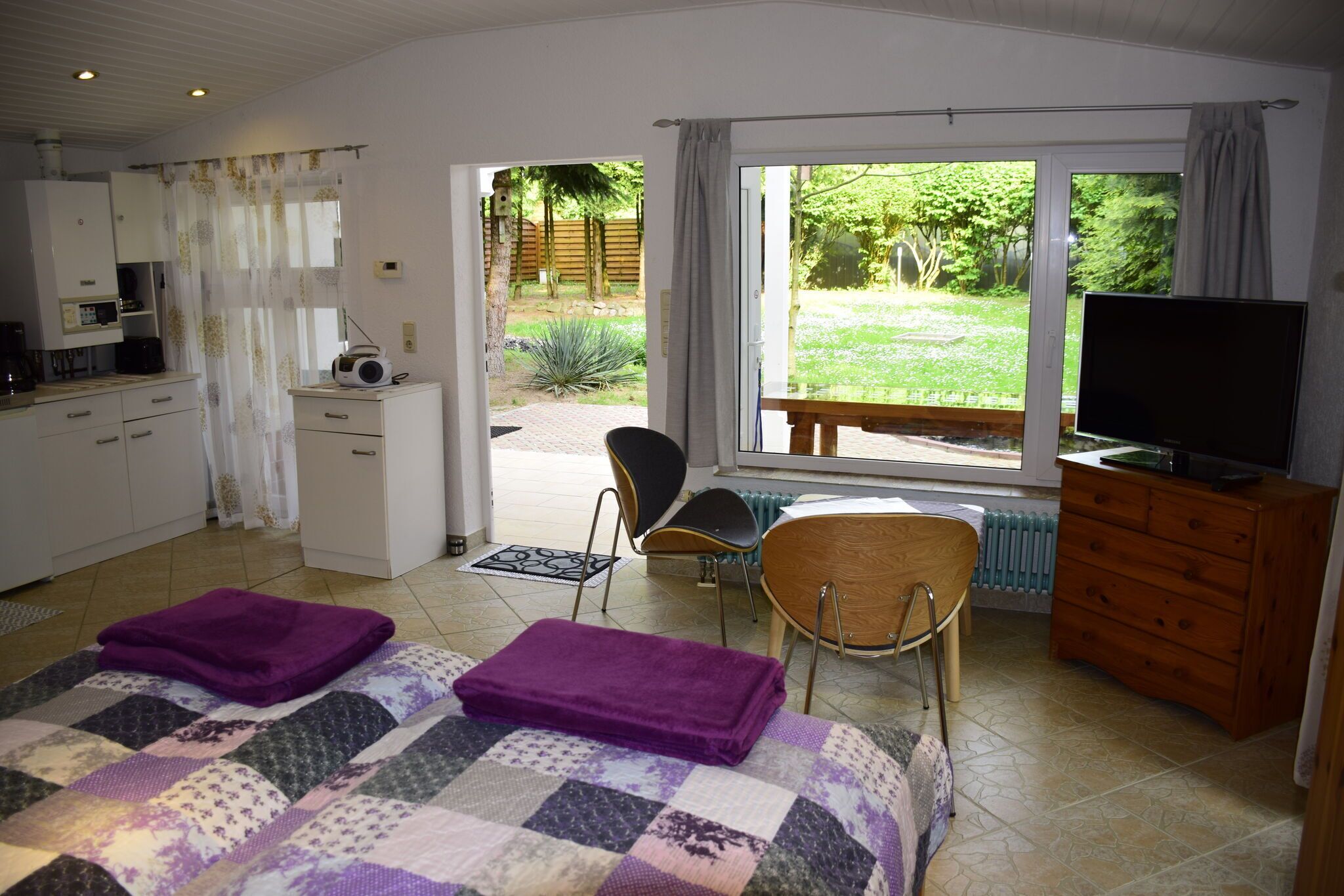 Een slaapkamer met een bed, een televisie, een houten dressoir en uitzicht op een tuin.