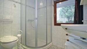 Een badkamer met een toilet, een douche met glazen wanden en een raam met uitzicht op bomen.