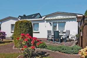 A white house with a covered patio, a large tree, and a garden with red flowers. - Ferienhäuser am Teich, Zinnowitz (Zinnowitz)