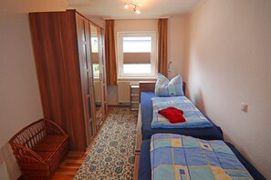 A small, narrow room with a single bed, a wooden wardrobe, a radiator, and a window with curtains. - Ferienhäuser am Teich, Zinnowitz (Zinnowitz)