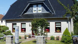 A two-story house with a steeply pitched roof, dormer windows, and a small garden with potted plants. - Ferienhäuser am Teich, Zinnowitz (Zinnowitz)