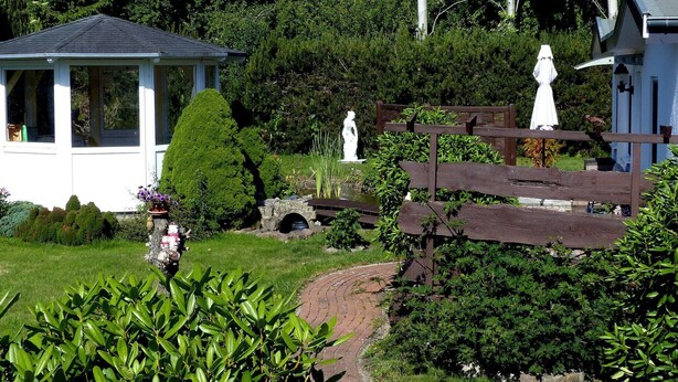 A garden with a gazebo, statues, and a wooden bridge. - Ferienhäuser am Teich, Zinnowitz (Zinnowitz)