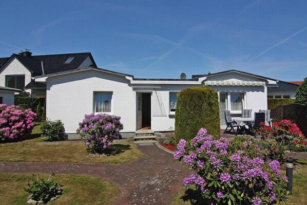 A white two-story house with a paved driveway, a well-maintained garden with purple flowers, and a neatly trimmed hedge. - Ferienhäuser am Teich, Zinnowitz (Zinnowitz)