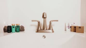 Un baño con un grifo moderno, un lavabo y diversos artículos de aseo, incluyendo champú, acondicionador y jabones.