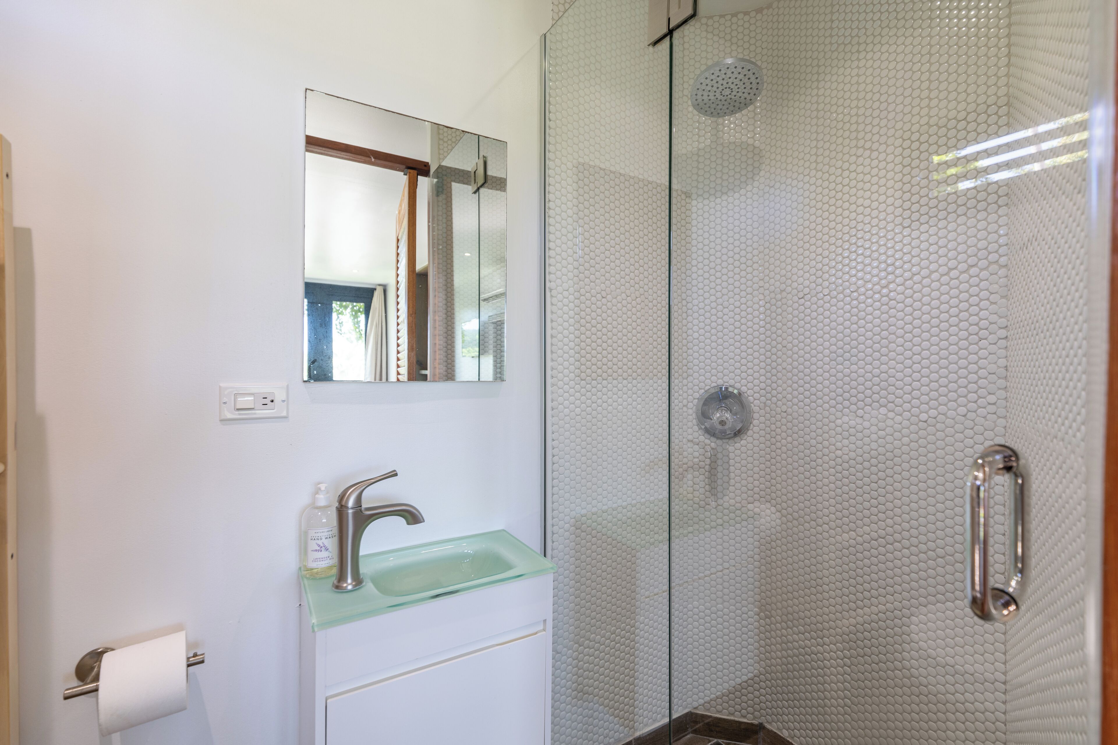 Een badkamer met een glazen douchecabine, een glazen wastafel en een spiegel boven de wastafel.