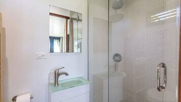 Een badkamer met een glazen douchecabine, een glazen wastafel en een spiegel boven de wastafel.