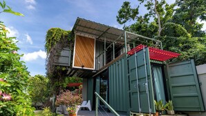 Une maison moderne avec une façade verte, une terrasse en bois et un toit rouge.