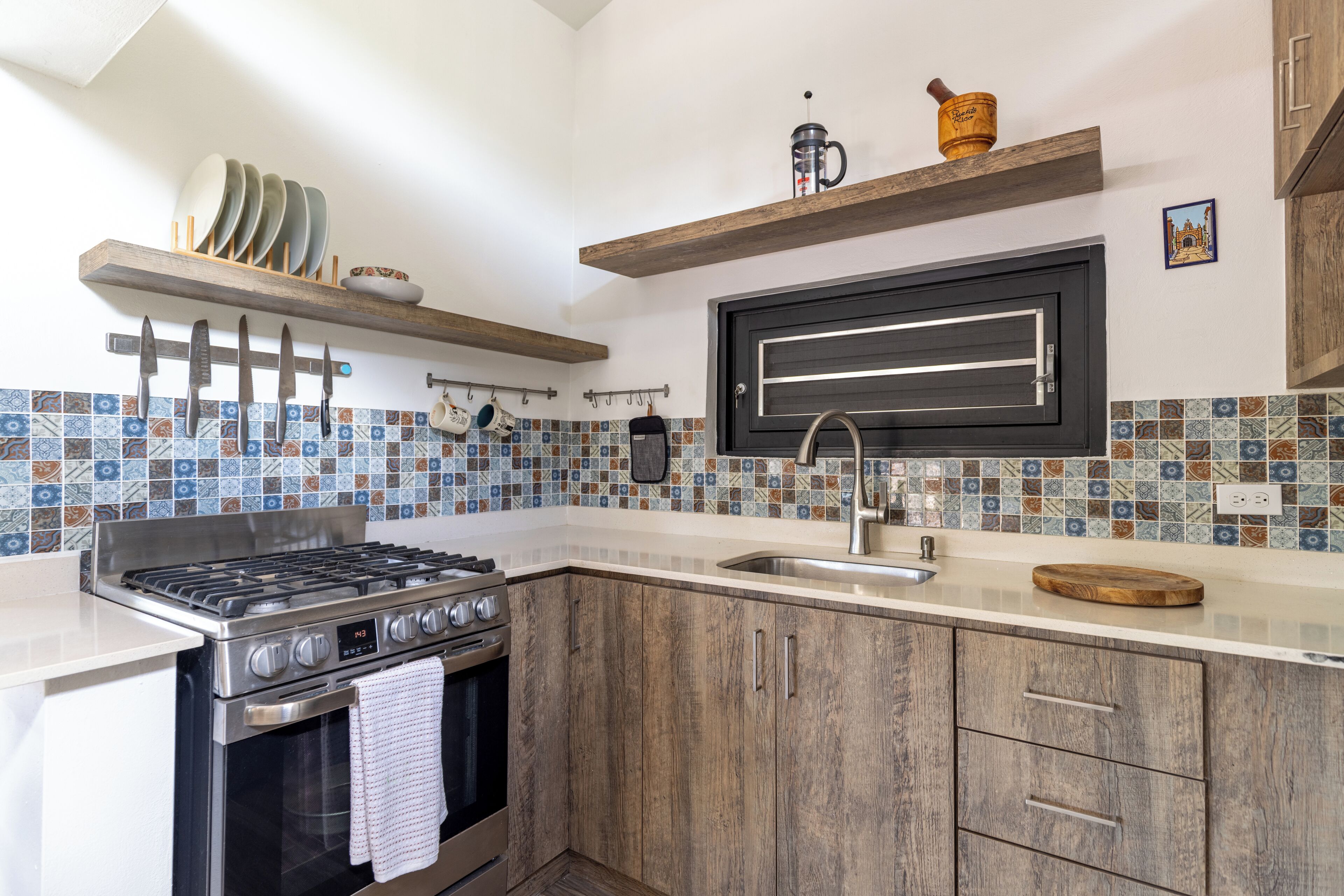 A kitchen with a stove, oven, sink, and wooden cabinets. There are hanging utensils and a coffee maker on the wall.