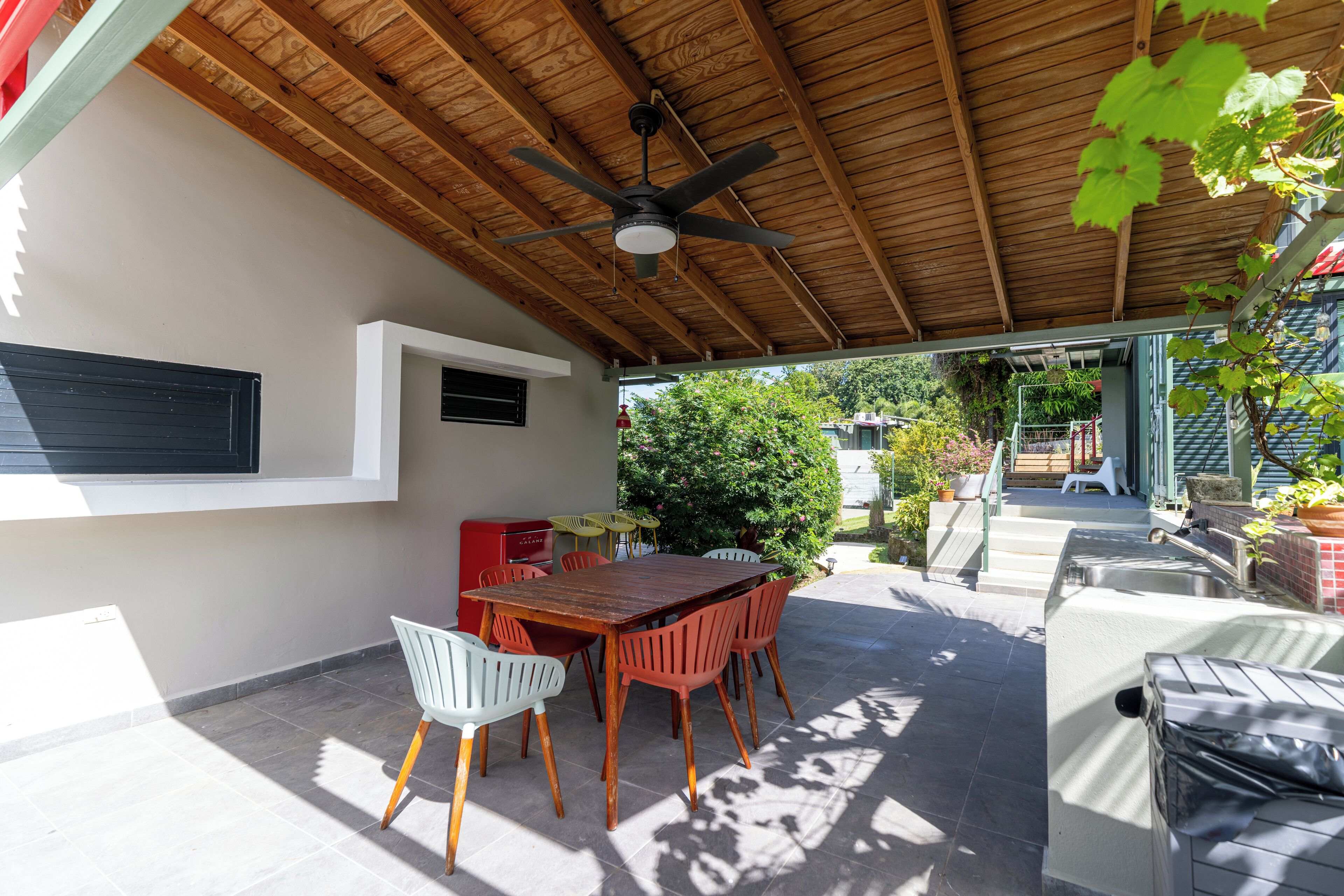An outdoor patio with a wooden ceiling, a dining table with chairs, and a barbecue grill.