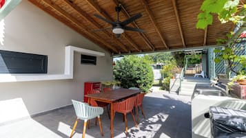 An outdoor patio with a wooden ceiling, a dining table with chairs, and a barbecue grill.