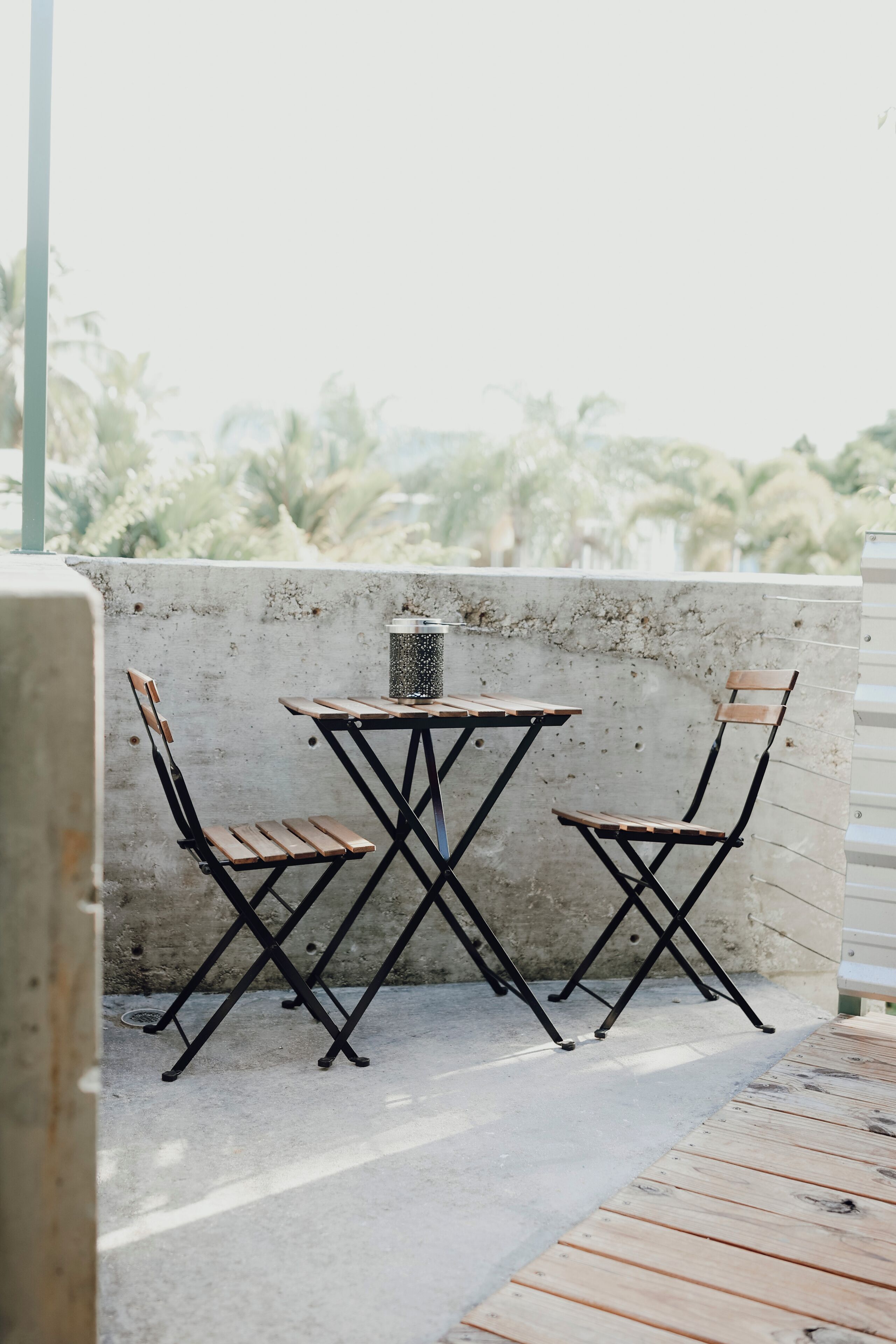 Un petit espace extérieur aménagé avec une table et deux chaises, une poubelle en métal et un mur en béton.