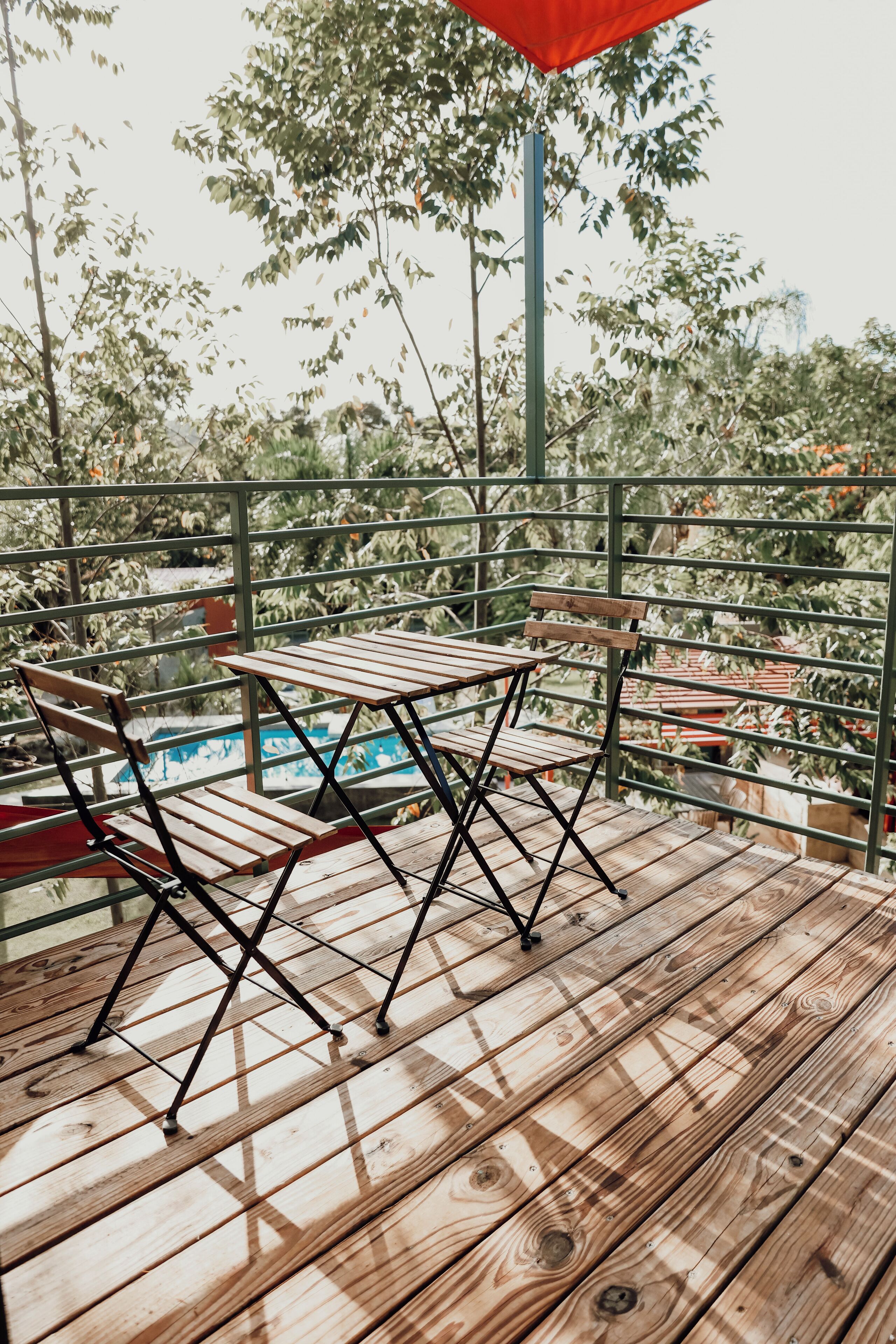 A wooden deck with a table and chairs, overlooking a pool and greenery.