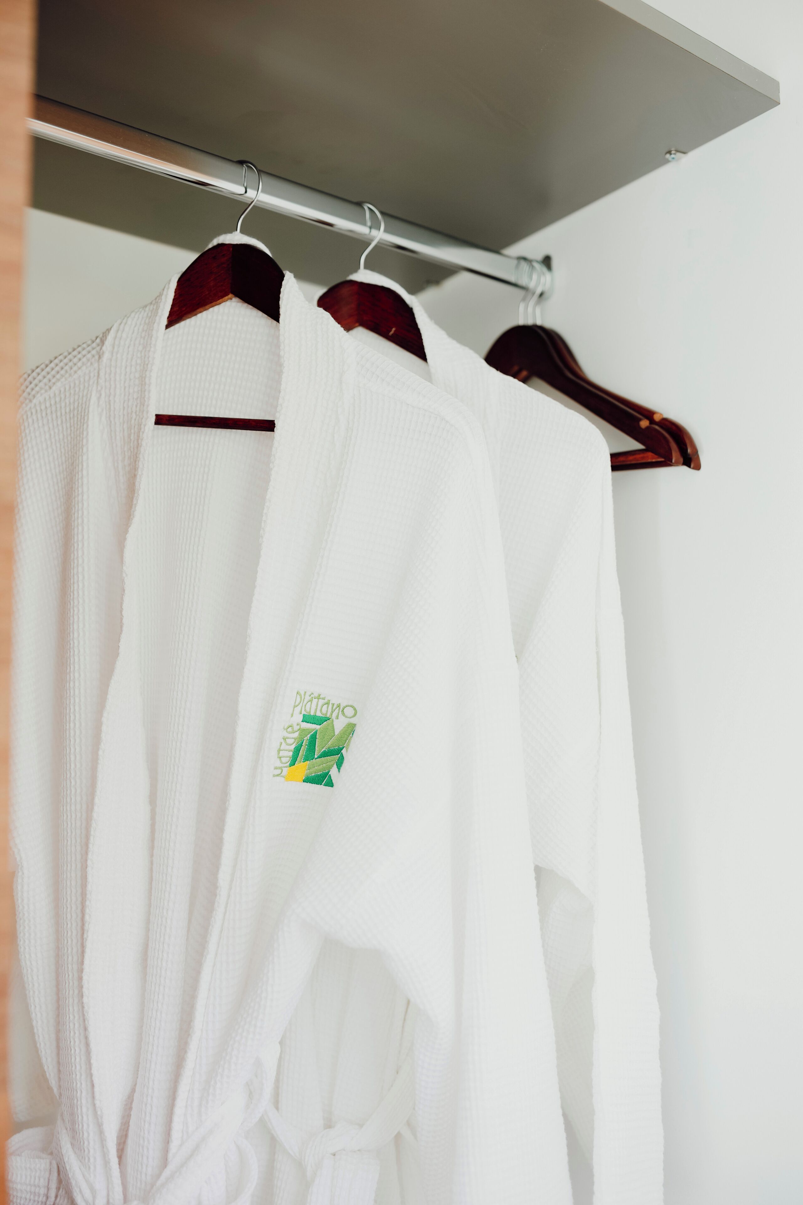 A closet with two white robes hanging on wooden hangers.