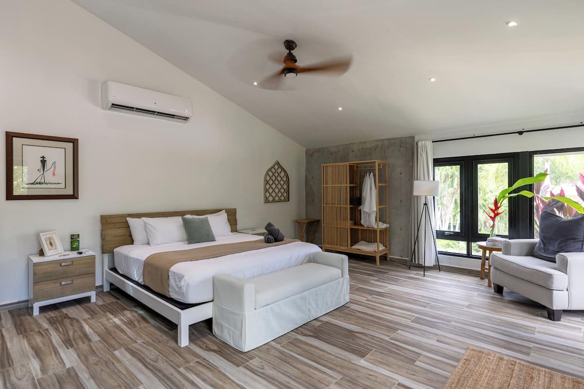 A modern bedroom with a bed, bedside table, bench, and a view of the outdoors through large windows.