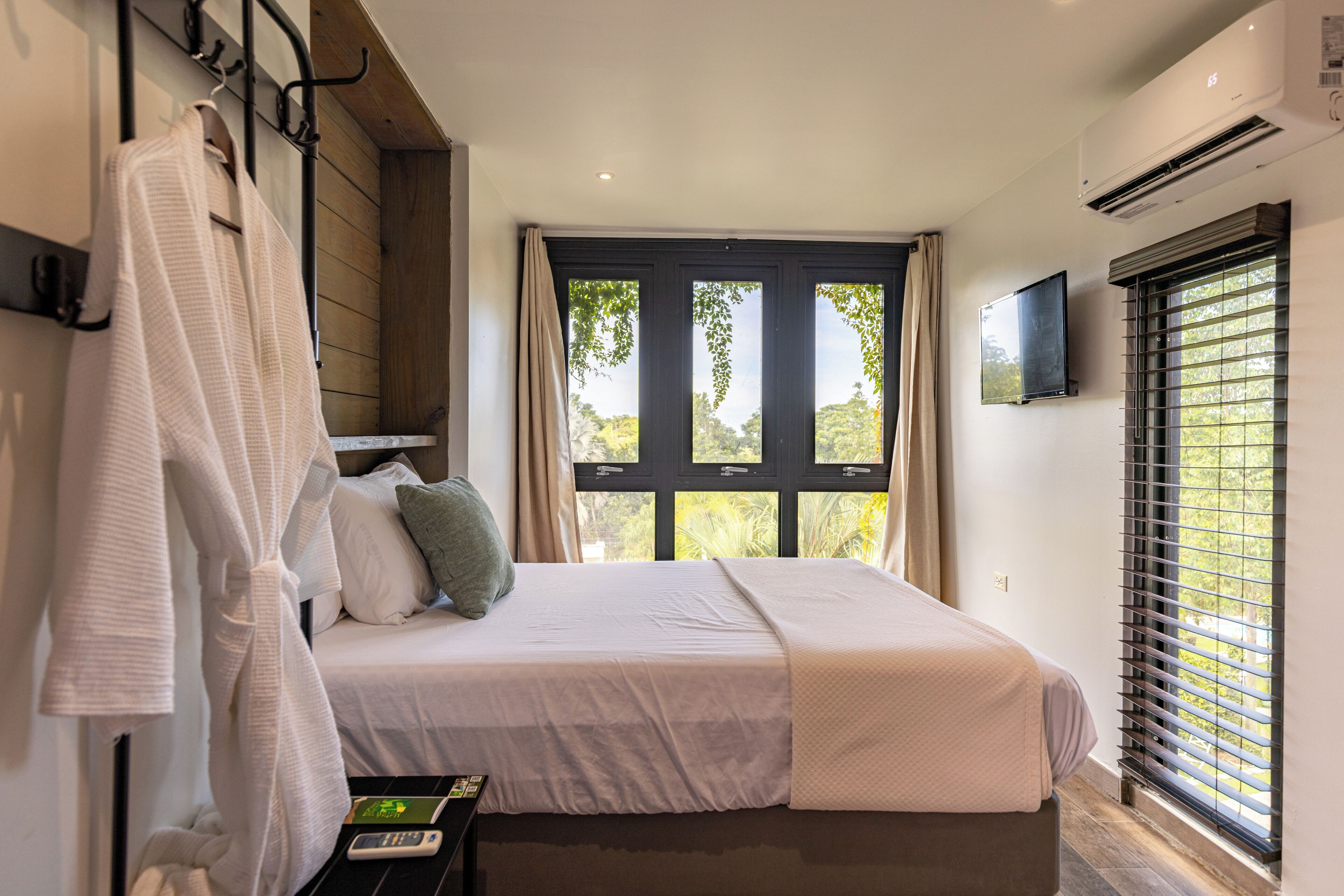 Un dormitorio con una cama, televisión, ventana con persianas y un perchero para toallas.