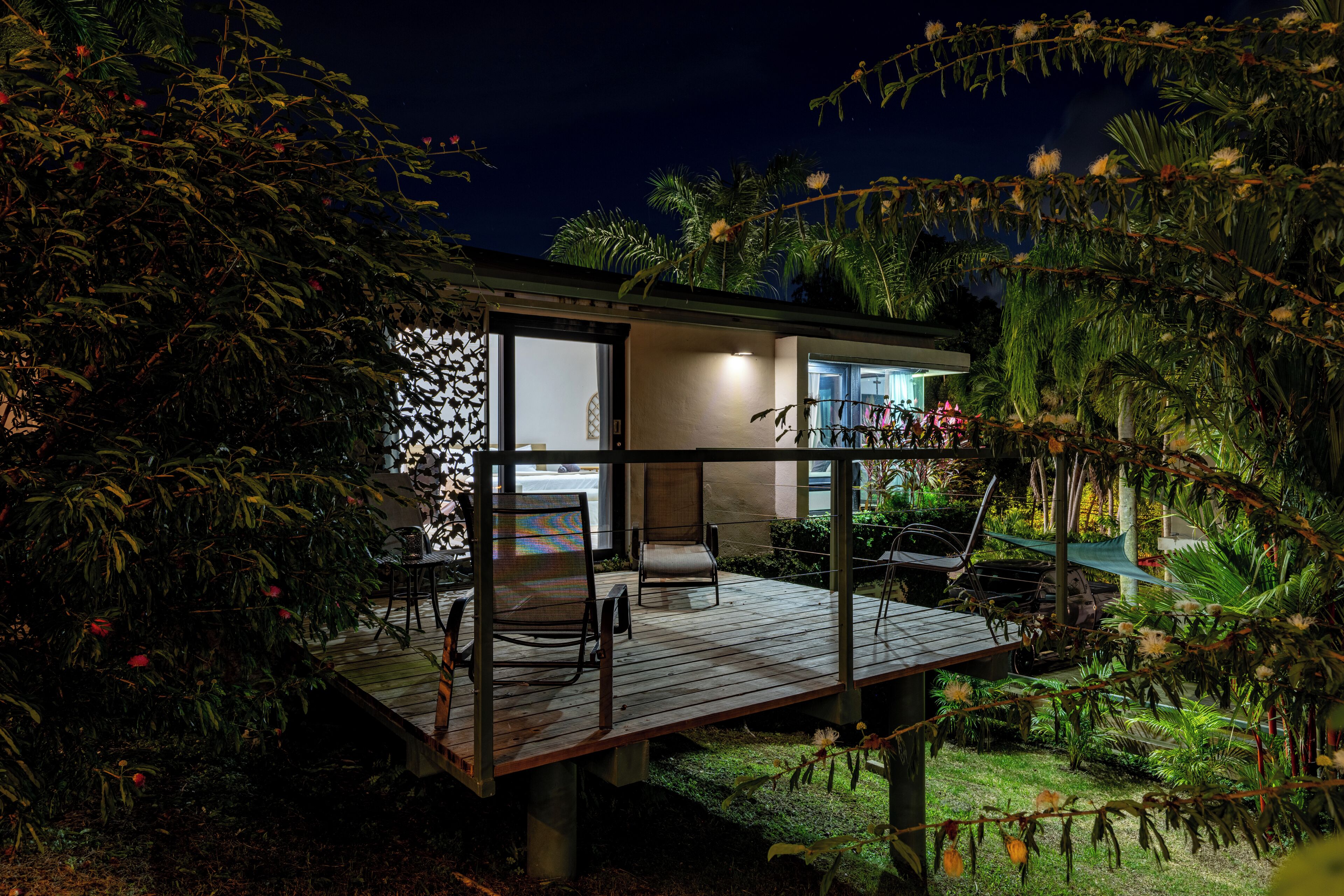A modern house with a wooden deck, a glass door leading to a room, and a hammock.