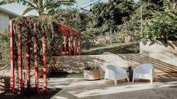 A patio area with a concrete floor, a red pergola covered in vines, a potted plant, and two white chairs under a red canopy.