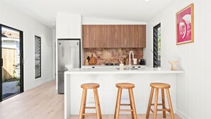 Une cuisine moderne avec des meubles blancs, un pare-feu en marbre et un îlot central doté de tabourets.