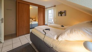 A bedroom with a large bed, a bedside table, a wardrobe, and a window with curtains. - Ferienwohnung im OG in Friedrichkoog-Spitze (Friedrichskoog-Spitze)